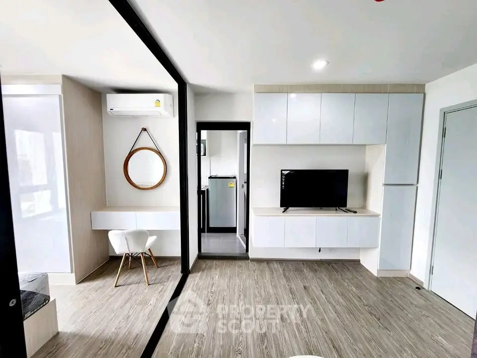 Modern living room with sleek design, featuring a wall-mounted TV, stylish mirror, and compact kitchen area.