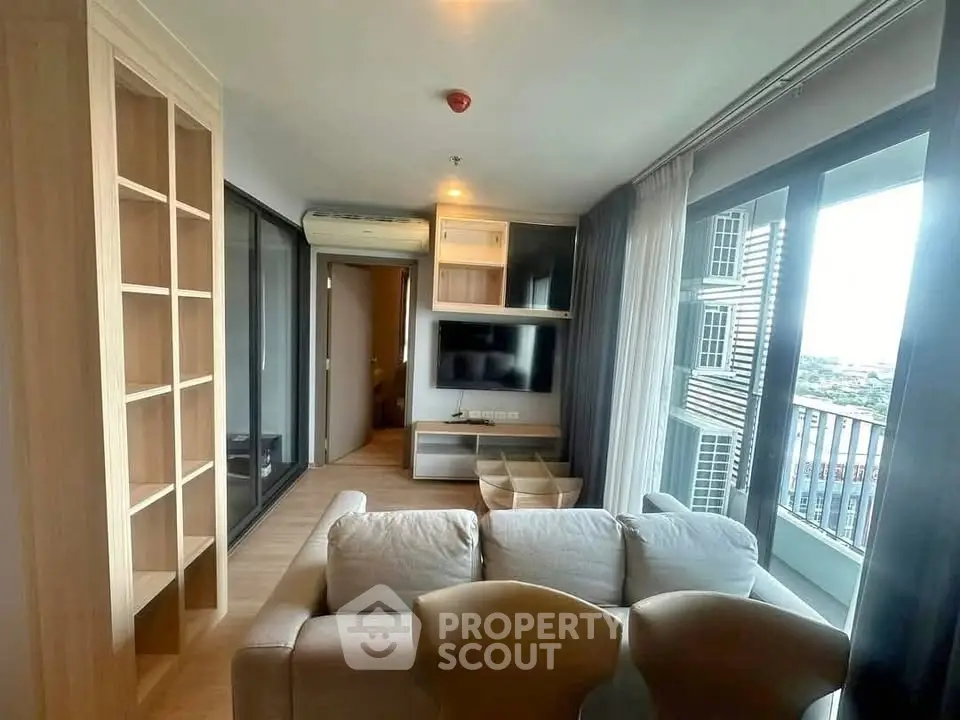 Modern living room with large windows and city view, featuring stylish furniture and built-in shelving.