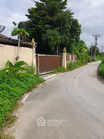 Charming suburban property with gated entrance and lush greenery along a quiet road.
