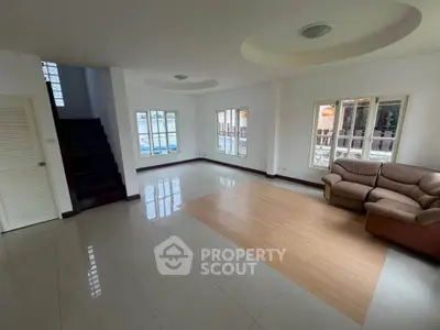 Spacious living room with modern design and ample natural light, featuring a cozy sofa and elegant staircase.