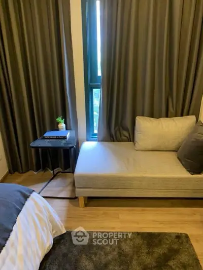 Cozy bedroom with modern decor and natural light, featuring a stylish chaise lounge and elegant curtains.