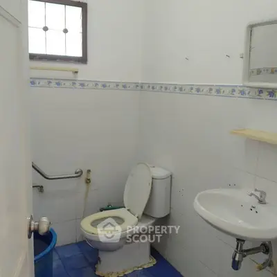 Simple bathroom with white tiles and blue floor, featuring a toilet and sink.