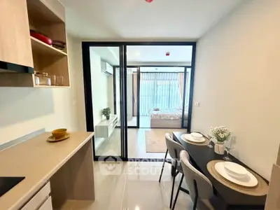 Modern open-plan kitchen and dining area leading to a cozy bedroom with glass partition.