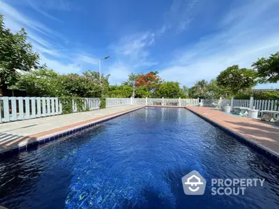 Stunning outdoor pool with lush greenery and clear blue sky, perfect for relaxation.