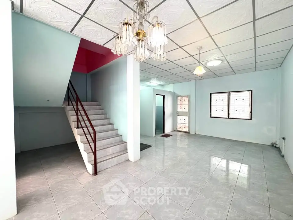 Spacious open-plan living area with elegant chandelier and staircase, perfect for modern family living.