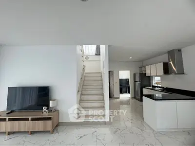 Modern open-plan living area with sleek kitchen and stylish staircase in a contemporary home.