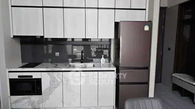 Modern kitchen with sleek cabinetry and marble countertops, featuring a built-in microwave and stylish fridge.