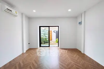 Spacious empty room with wooden flooring and large sliding glass door leading to garden.