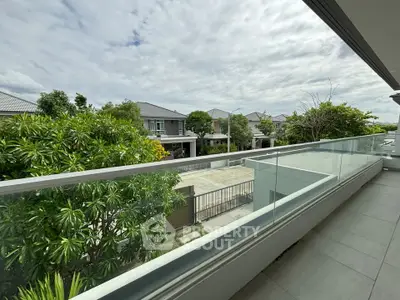 Spacious balcony with glass railing offering a serene view of modern suburban homes and lush greenery.