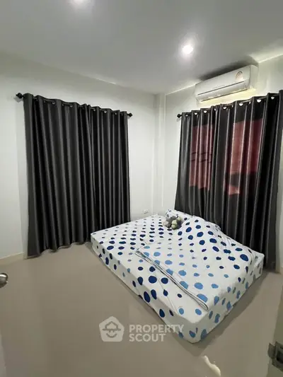 Cozy bedroom with minimalist decor and air conditioning, featuring dark curtains and a comfortable mattress.