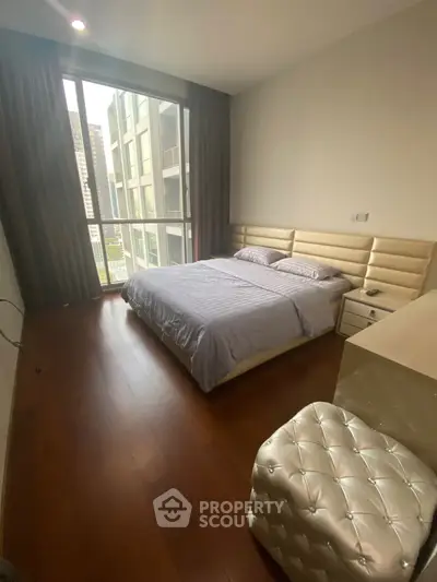 Modern bedroom with large window and stylish decor in urban apartment.