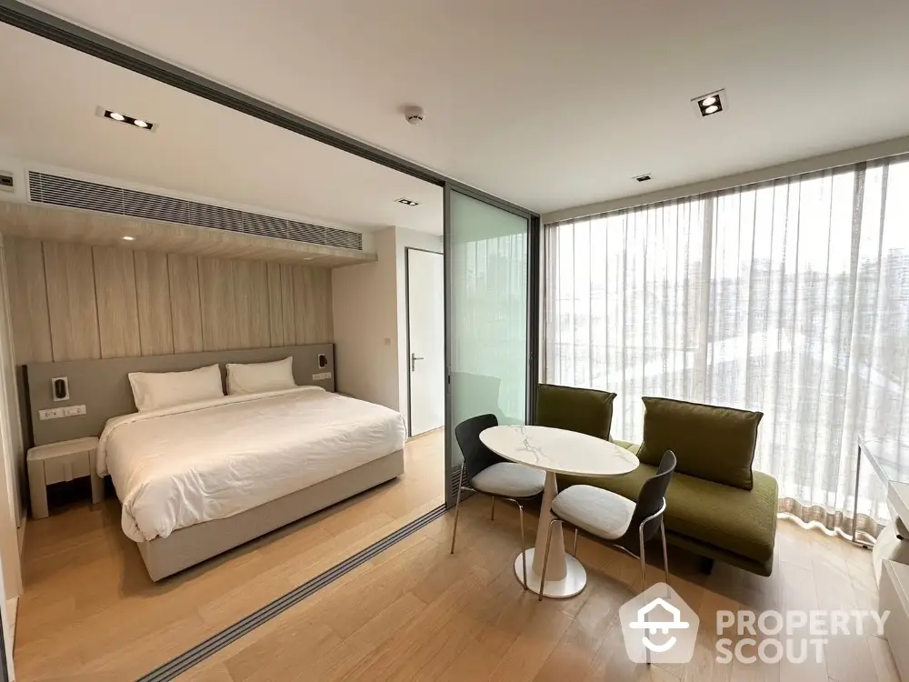 Modern studio apartment with glass partition, cozy bed, and stylish seating area.