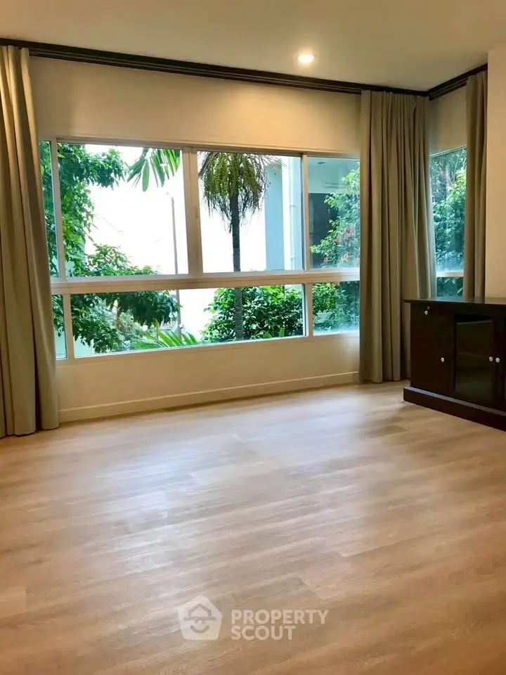 Spacious living room with large window and garden view, perfect for natural light lovers.