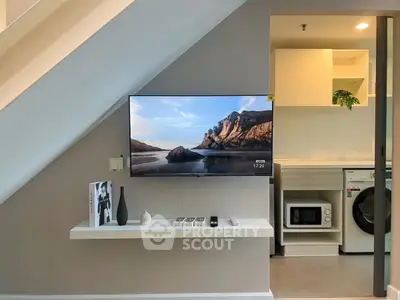 Modern living space with TV, shelf, and compact kitchen appliances under staircase.