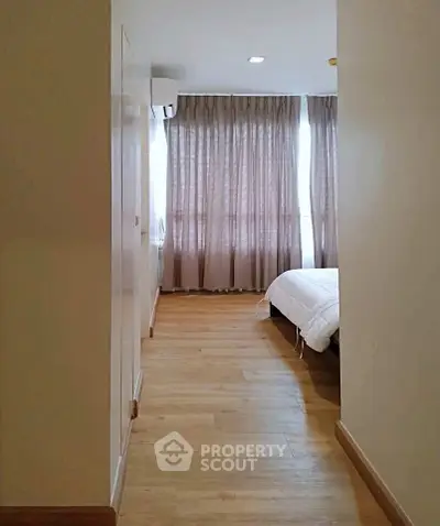 Spacious bedroom with wooden flooring and large windows for natural light.