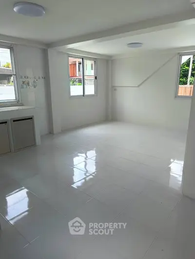 Spacious and bright empty room with large windows and glossy white tile flooring.
