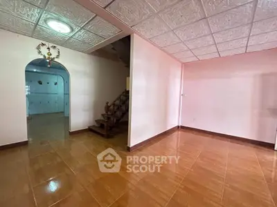 Spacious interior with tiled floors and decorative ceiling, featuring a staircase and archway leading to another room.