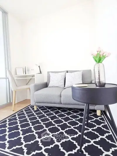 Modern living room with stylish gray sofa, elegant black table, and chic patterned rug.