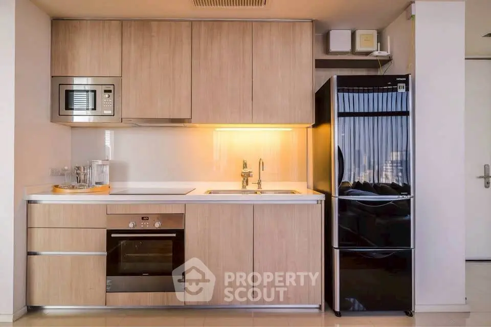 Modern kitchen with sleek wooden cabinets, built-in oven, microwave, and black fridge in a stylish apartment.