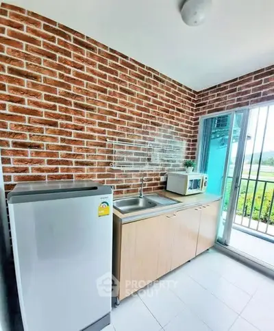 Modern kitchen with brick wall, stainless steel sink, fridge, and microwave near balcony.