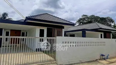 Modern single-story house with tiled roof and gated entrance, surrounded by lush greenery.