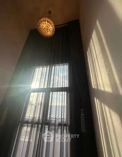 Elegant high ceiling window with luxurious chandelier and sheer curtains, showcasing natural light and modern design.