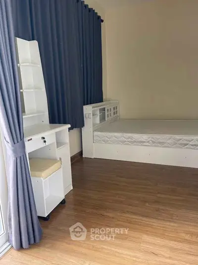 Cozy bedroom with wooden flooring, single bed, and study desk near window with blue curtains.