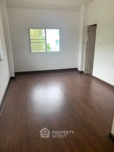 Spacious empty room with wooden flooring and large window, ideal for customization.