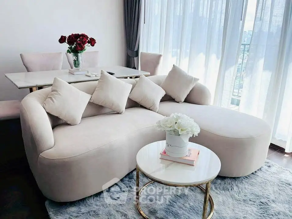Elegant living room with plush sofa, chic coffee table, and dining area by large windows.
