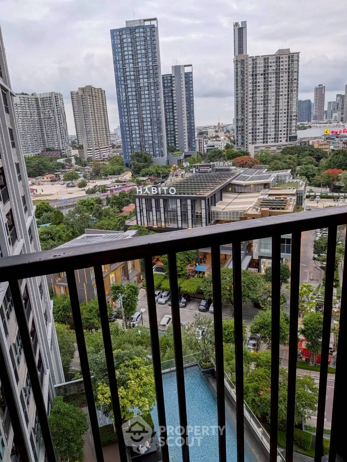 Stunning cityscape view from a high-rise balcony overlooking a pool and modern buildings.