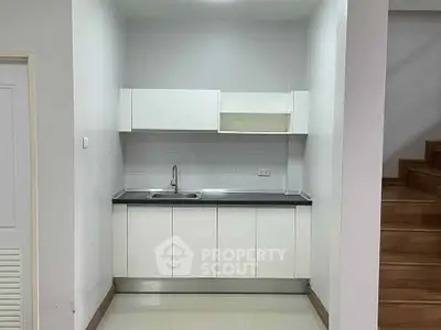 Compact kitchen with sleek white cabinets and modern sink, adjacent to wooden staircase.