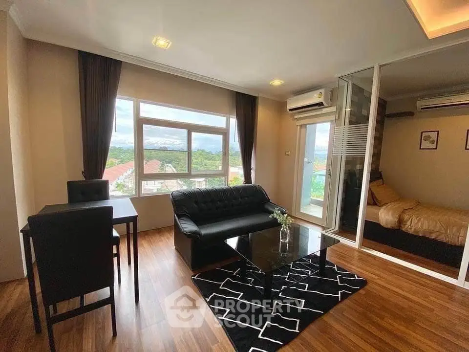 Modern living room with sleek black sofa and glass coffee table, adjacent to cozy bedroom with natural light.