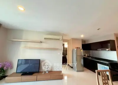 Modern living room with sleek kitchen, featuring TV, air conditioning, and stainless steel fridge.