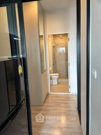 Modern apartment hallway leading to a compact bathroom with glass shower enclosure.