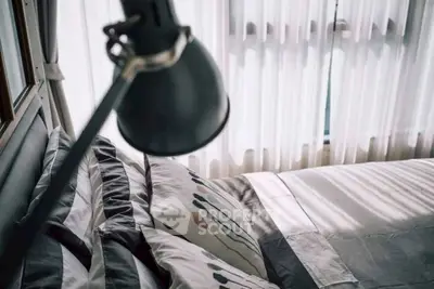 Cozy bedroom with stylish bedding and natural light through sheer curtains.