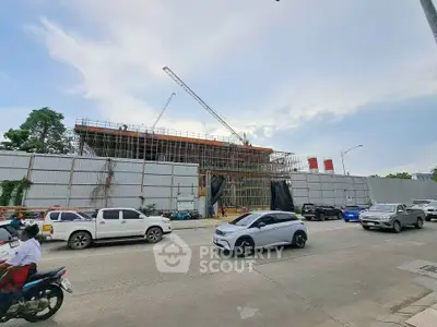 Construction site of a modern building with cranes and vehicles on a busy street.