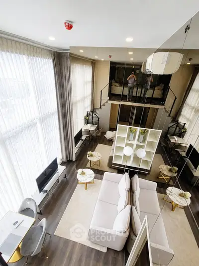 Luxurious modern living room with high ceilings and mezzanine, featuring elegant decor and ample natural light.