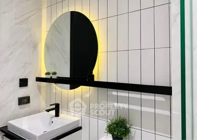Modern bathroom with illuminated round mirror and sleek black fixtures.