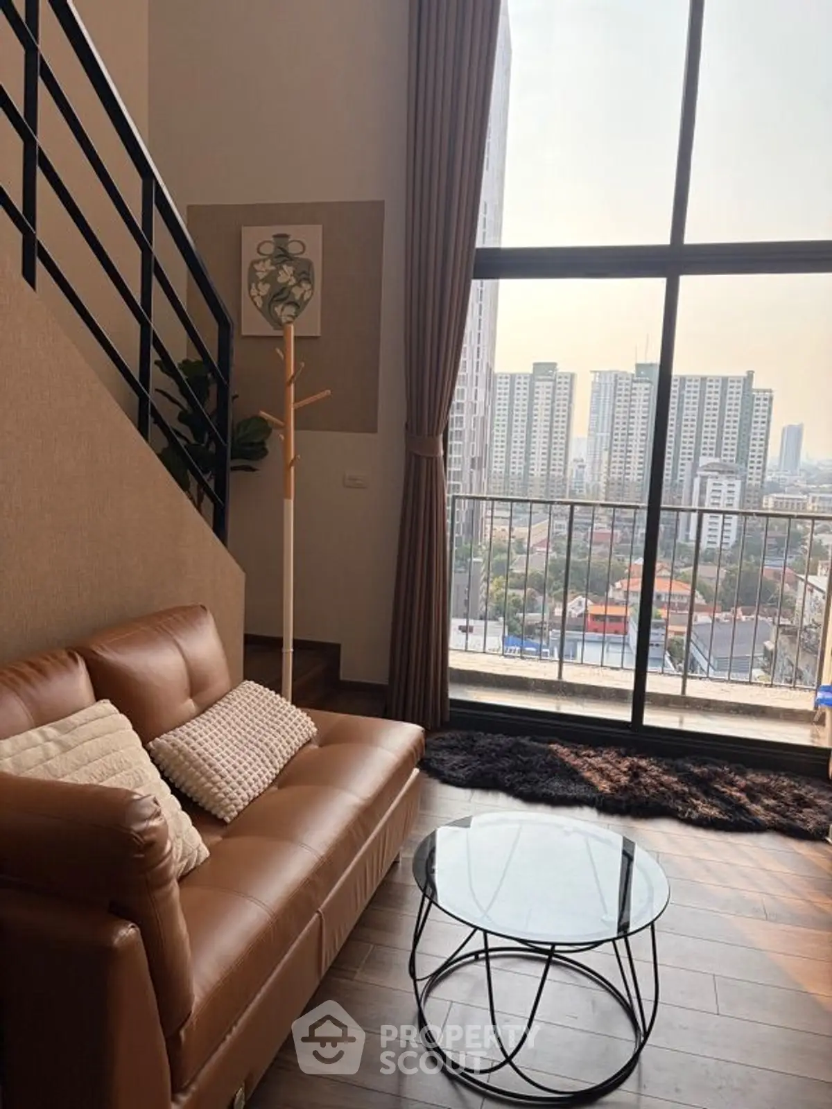 Modern living room with large windows and city view, featuring stylish sofa and glass coffee table.