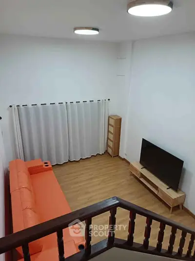 Modern living room with orange sofa, flat-screen TV, and wooden flooring, perfect for cozy family gatherings.