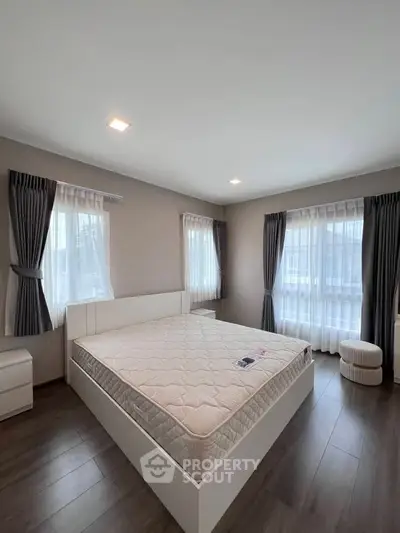 Spacious bedroom with large windows and elegant curtains, featuring a comfortable bed and modern decor.
