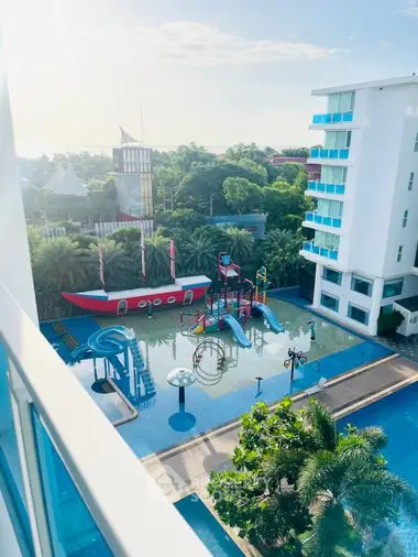 Inviting family-friendly condominium complex with a vibrant children's pool area, complete with slides and play structures, surrounded by lush greenery and modern buildings.