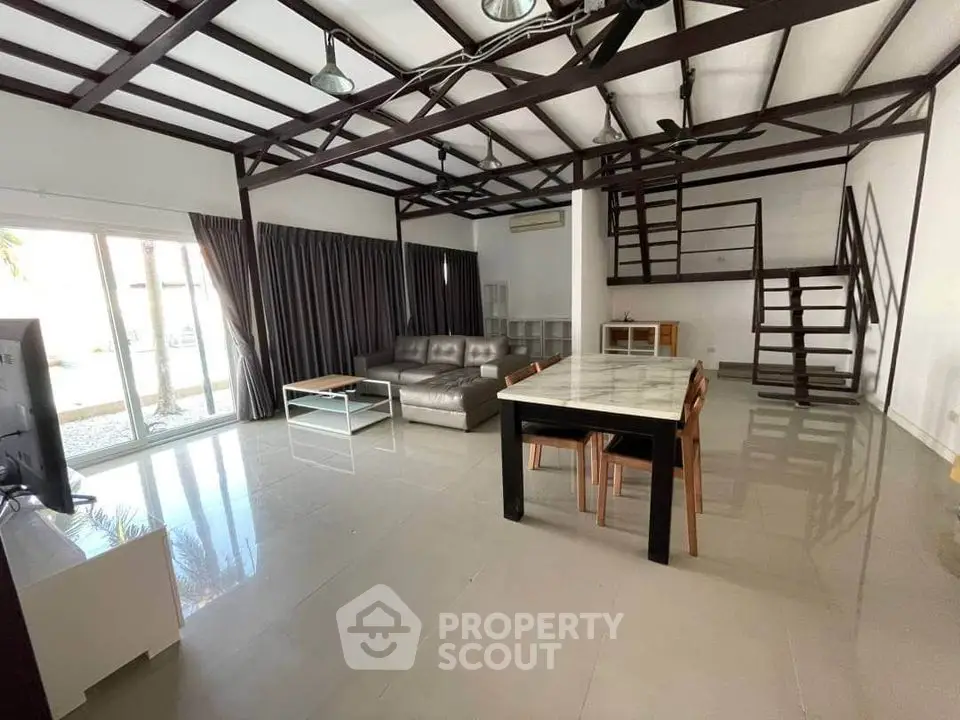 Spacious living room with high ceilings, exposed beams, and glossy tiled floors, featuring large windows for ample natural light.