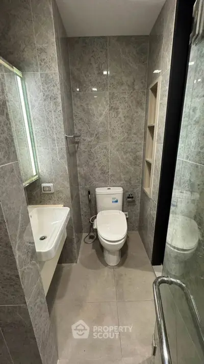 Modern bathroom with sleek gray tiles and contemporary fixtures, featuring a toilet, sink, and shower area.