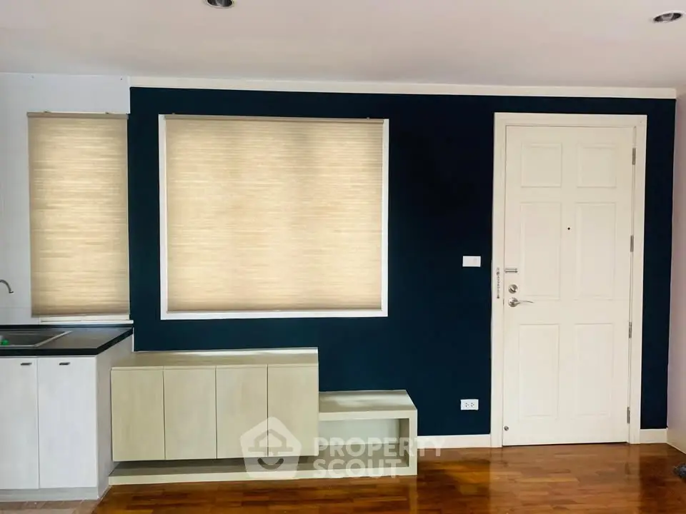 Modern interior with navy accent wall and white door, featuring sleek cabinetry and hardwood floors.