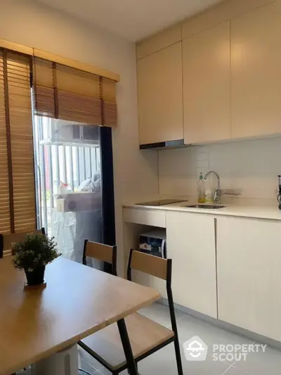 Modern kitchen with sleek cabinets and dining area, featuring natural light and stylish decor.