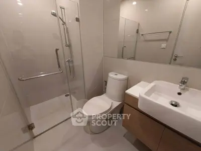 Modern bathroom with glass shower, sleek sink, and toilet in contemporary design.