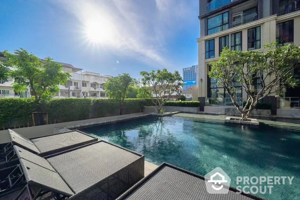 Luxurious apartment complex with serene pool and lush greenery under a bright blue sky.