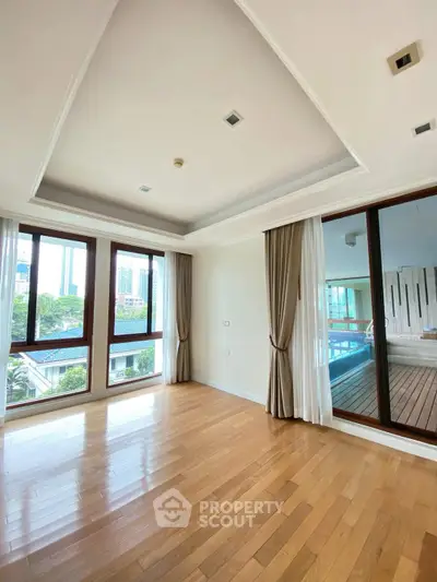 Spacious room with wooden floors and large windows offering city views