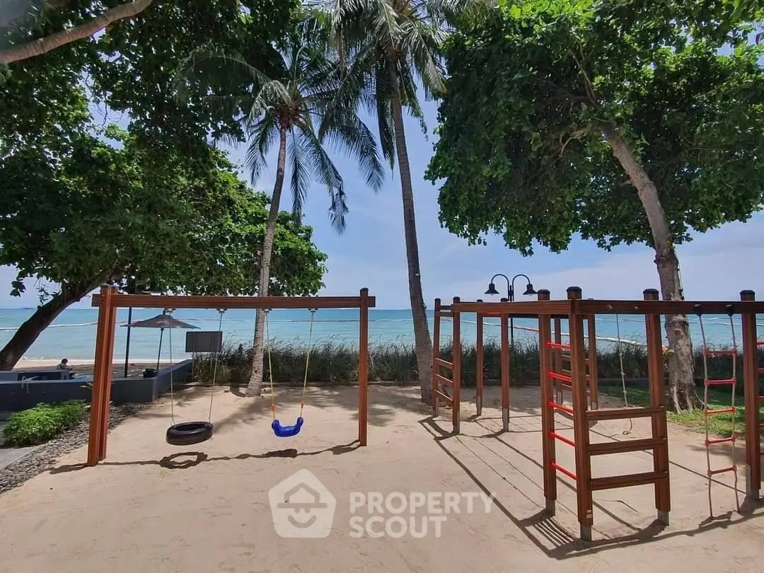 Beachfront playground with swings and climbing frames under palm trees.